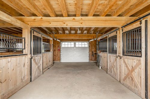 Barn aisle flanked by horse stalls leading to a closed garage door
