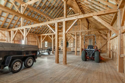 Barn interior with exposed timber trusses, a dump trailer and farm equipment