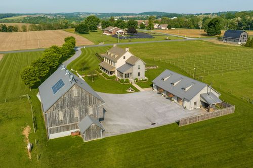 Aerial view of a farmhouse, barn and vineyard rows on a sunlit morning