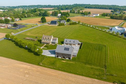 Aerial view of a farmhouse and barn with rooftop solar panels beside the driveway