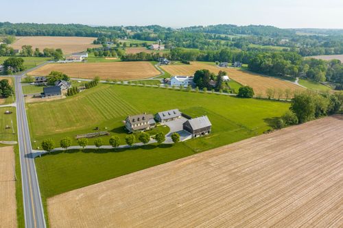 Aerial view of a farmhouse and barn along a country road lined with trees