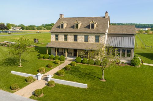 Aerial close-up of a stone farmhouse with multiple chimneys beside a matching barn