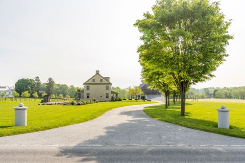 White gate pillars mark a curving driveway leading to a stone farmhouse and barn