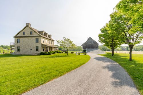 Stone farmhouse and barn viewed from the driveway beneath a mature shade tree