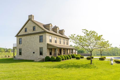 Two-story stone farmhouse exterior with dormer windows and manicured shrubs