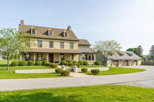 Stone and stucco farmhouse exterior with a covered porch and attached garage wing