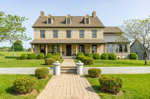 Front exterior of a stone farmhouse with a covered porch and brick walkway