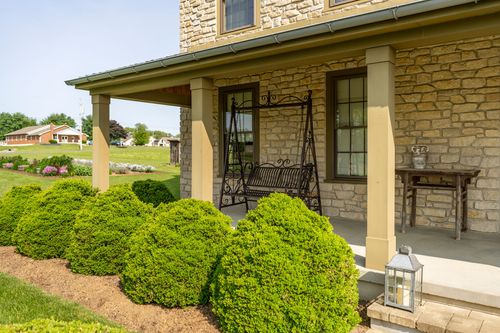 Covered stone porch with columns, an iron bench swing and a side table
