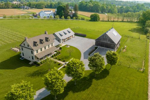 Aerial view of a farmhouse and barn along a tree-lined driveway with a distant grain silo