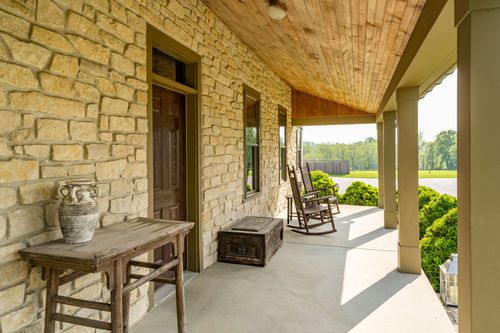 Covered porch with a wood-paneled ceiling, rocking chairs and an antique trunk