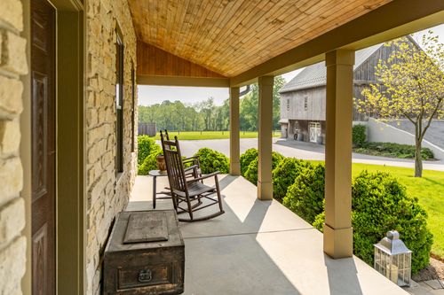 Covered stone porch corner with rocking chairs overlooking the lawn and barn