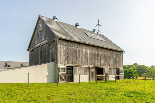 Weathered barn roof fitted with solar panels and a wind turbine