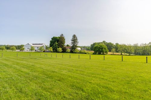 Open pasture with fence posts leading toward a distant farmhouse and barn