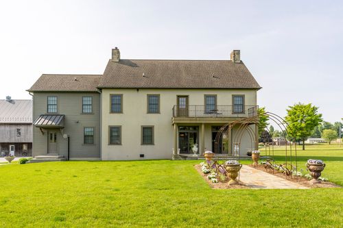 Rear exterior of a stone farmhouse with a balcony overlooking garden arbors