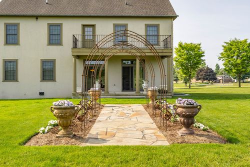 Garden path lined with iron arbor trellises and flower-filled urns leading to the porch