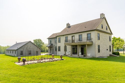 Rear exterior of a two-story farmhouse with a stone balcony overlooking the garden