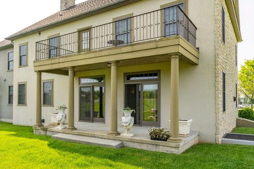 Covered stone patio beneath an iron balcony with French doors and potted plants