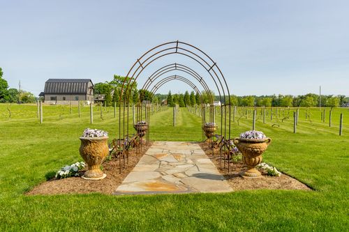 Garden walkway beneath a row of iron arch trellises flanked by flowering urns