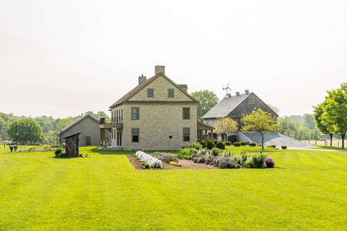 Farmhouse and weathered barn with a mulched garden bed and small shed