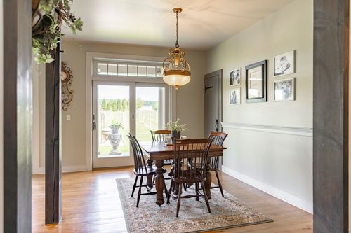 Dining room table set beneath a chandelier, kitchen with hanging herbs beyond