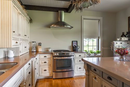 Gas range beneath hanging dried herbs in a white farmhouse kitchen