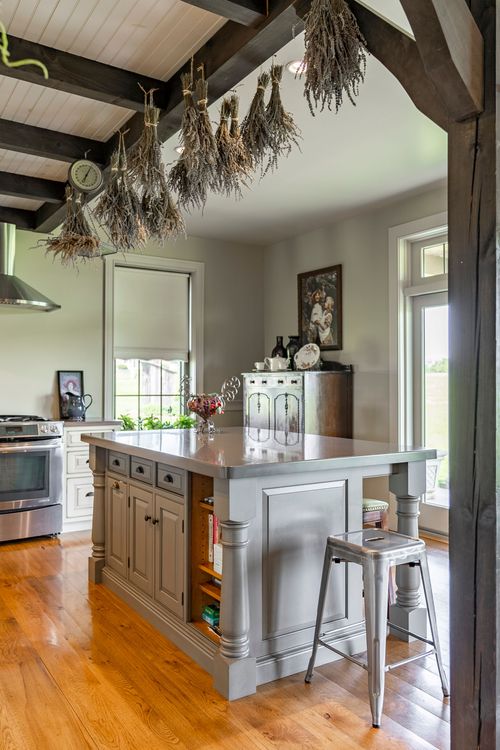 Kitchen island with iron stools beneath dried herbs hanging from dark beams