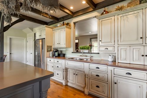 White farmhouse kitchen with a stainless refrigerator and hanging dried herbs
