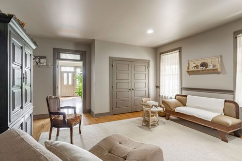 Sitting room with a dark armoire and wicker chair beside the open front door