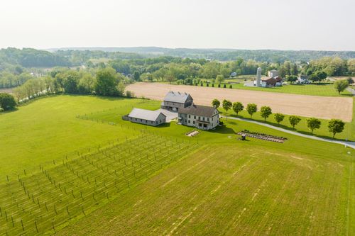 Aerial view of a farmhouse and barn beside vineyard rows and open farmland