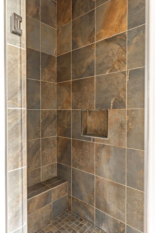 Walk-in tiled shower with stone-look tile and a built-in corner bench