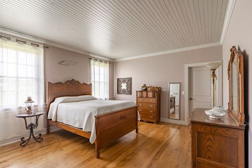 Bedroom with a wood bed, dresser and mirror beneath a beadboard ceiling