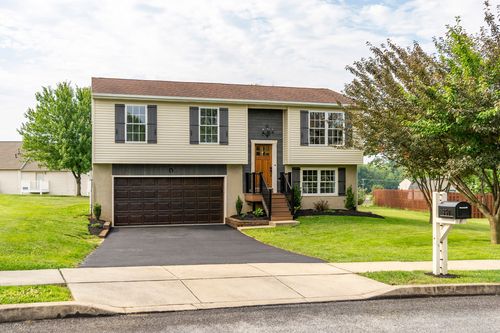 Split-level home with tan and dark siding, black shutters and a paved driveway