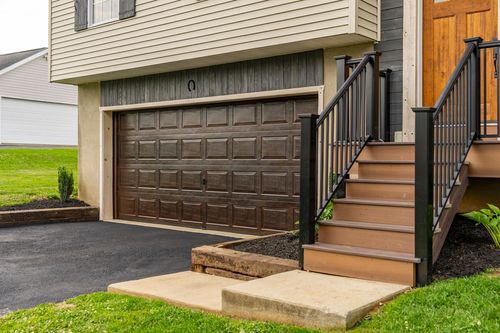 Garage and entry steps with a black metal railing and dark wood garage door