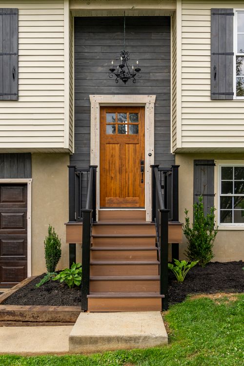 Front entry with a paneled wood door, black railings and landscaped beds