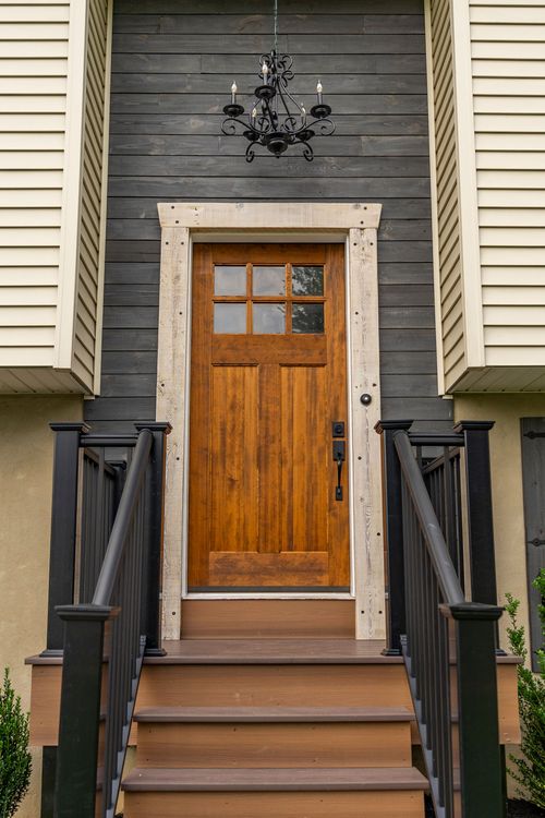 Wood entry door framed by dark shiplap siding and a hanging chandelier