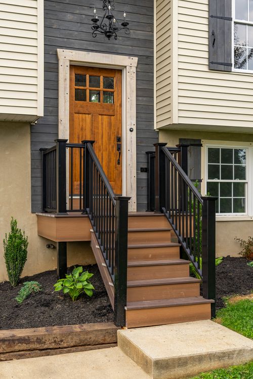 Front entry steps with black railings, a wood door and manicured shrubs
