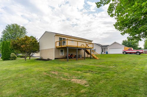 Rear exterior with an elevated deck, staircase and riding mower parked below