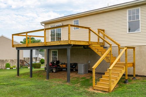 Rear elevated deck with a staircase, carport below housing a mower and AC unit