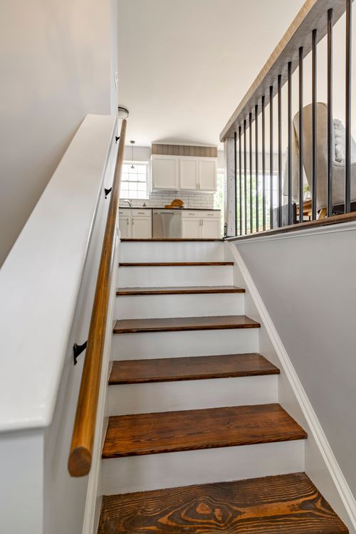 Staircase with dark wood treads and a wrought iron railing leading to an open kitchen