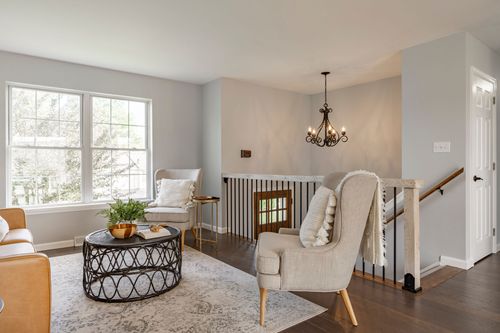 Living room chairs near the staircase landing with a chandelier overhead