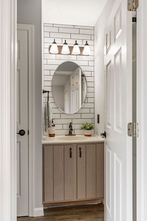 Bathroom with an oval mirror, subway tile wall and wood-tone vanity
