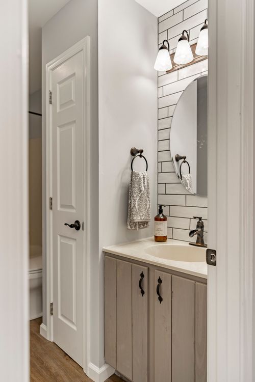 Powder room with a round mirror, subway tile accent wall and wood-tone vanity