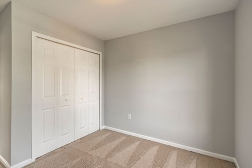 Empty bedroom with white bifold closet doors and neutral carpet