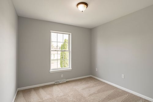 Empty bedroom with neutral carpet and natural light from a side window