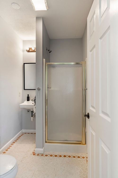 Bathroom with a gold-framed glass shower enclosure and patterned tile floor