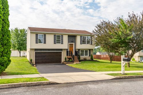 Split-level home exterior with tan siding, a dark garage door and covered entry steps