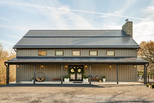 Barn-style venue exterior with a metal roof, stone chimney and a covered porch decorated with wreaths