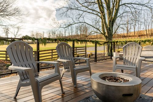 Outdoor deck with Adirondack chairs around a fire pit overlooking open pasture