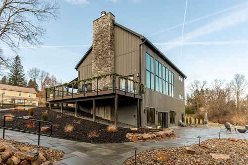 Rear exterior with a stone chimney, elevated deck and stone patio above a creek