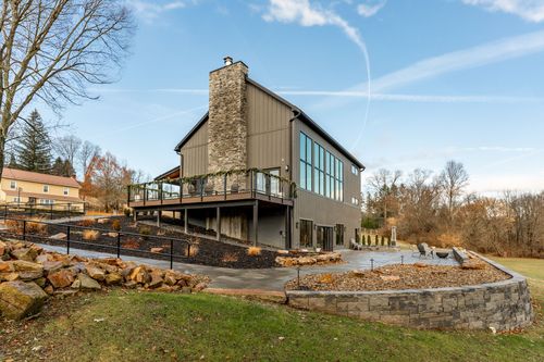 Rear exterior with a stone chimney, tall glass windows and a stacked stone wall